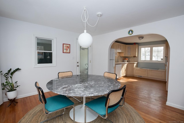 dining area featuring arched walkways, baseboards, and light wood finished floors