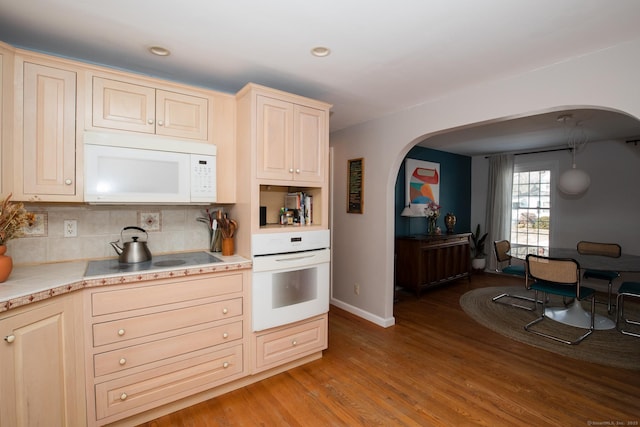 kitchen featuring arched walkways, light wood finished floors, light countertops, backsplash, and white appliances