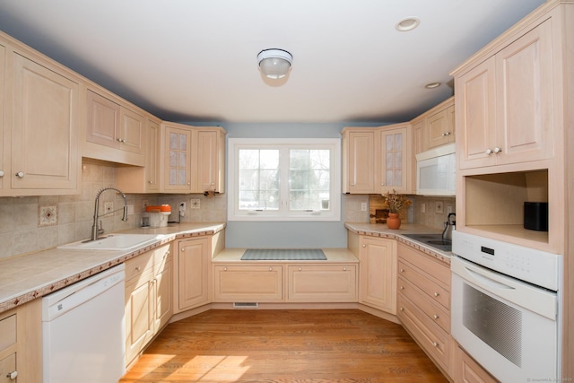 kitchen with white appliances, glass insert cabinets, light wood finished floors, and a sink