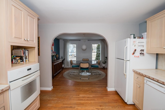 kitchen with white appliances, arched walkways, light wood-style flooring, light countertops, and light brown cabinets