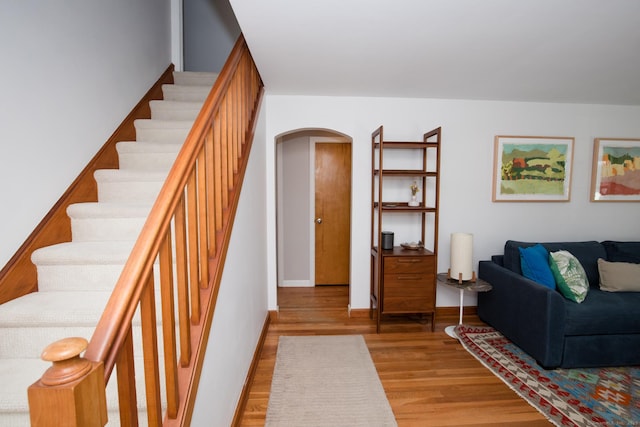 living room featuring stairway, arched walkways, light wood-style flooring, and baseboards