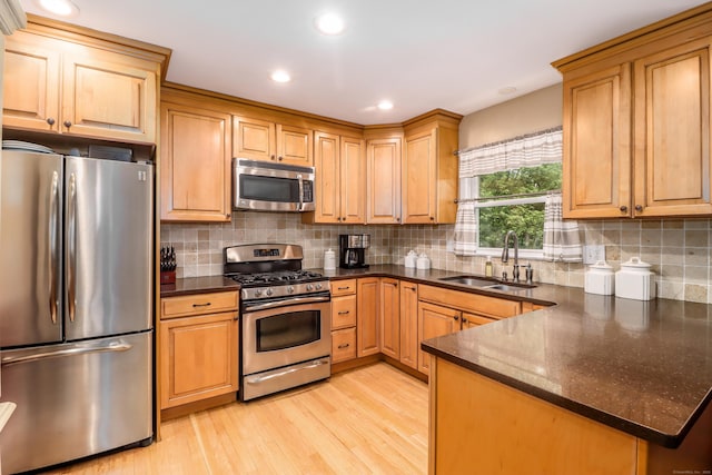 kitchen featuring light wood finished floors, appliances with stainless steel finishes, decorative backsplash, and a sink