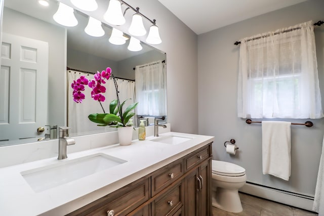 bathroom with toilet, double vanity, a baseboard heating unit, and a sink