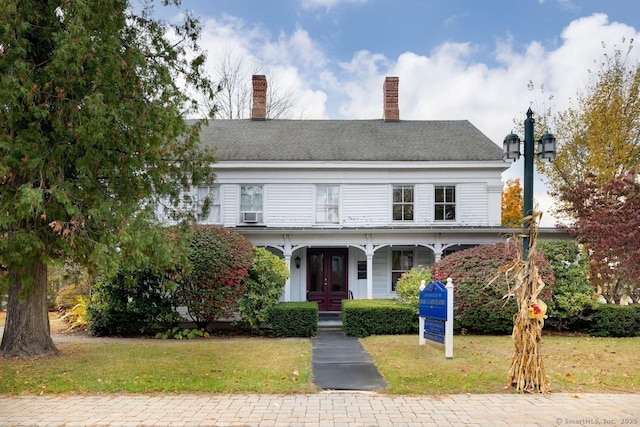 view of front facade with a shingled roof, a chimney, french doors, and a front yard