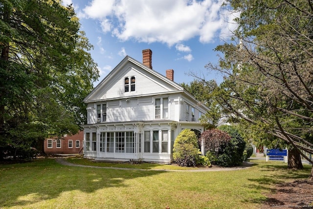 back of property featuring a sunroom, a lawn, and a chimney