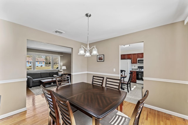 dining space featuring visible vents, baseboards, a chandelier, and light wood finished floors