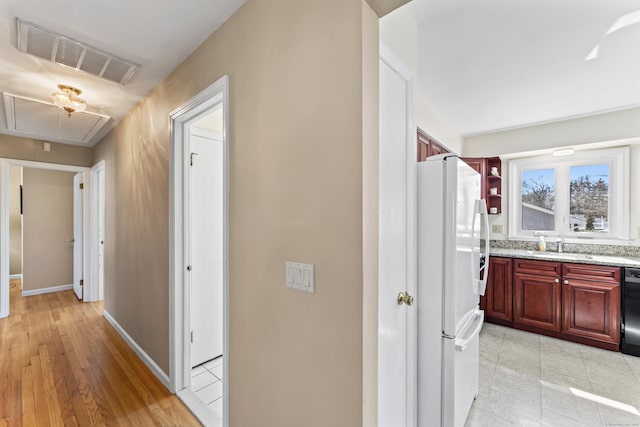 hallway featuring baseboards, visible vents, attic access, light tile patterned flooring, and a sink