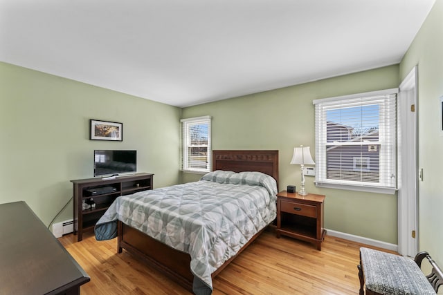 bedroom with a baseboard radiator, multiple windows, baseboards, and light wood finished floors