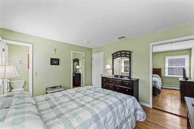 bedroom with baseboards, wood finished floors, visible vents, and a baseboard radiator