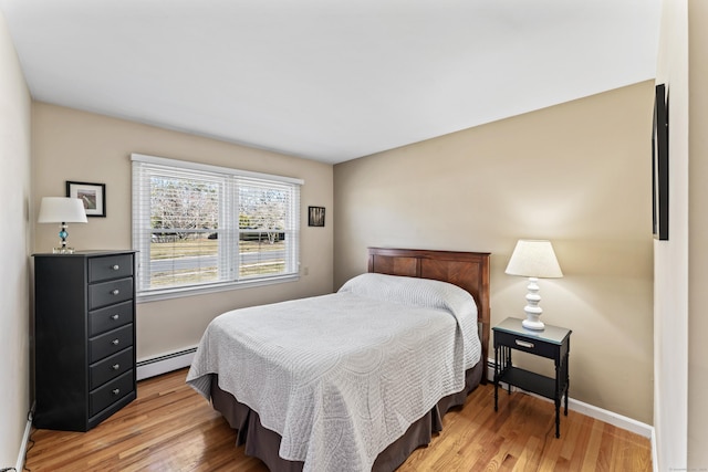 bedroom with a baseboard heating unit, baseboards, and light wood finished floors