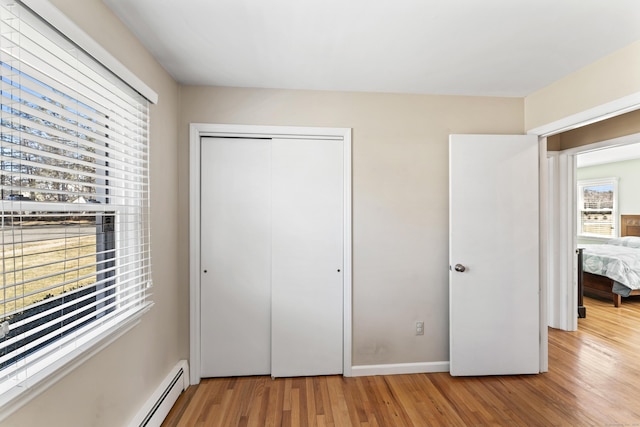 unfurnished bedroom with a closet, baseboard heating, baseboards, and wood finished floors