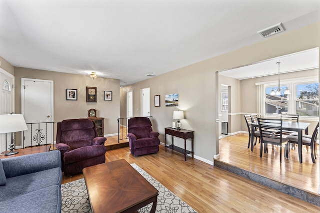 living room featuring an inviting chandelier, light wood-style flooring, baseboards, and visible vents