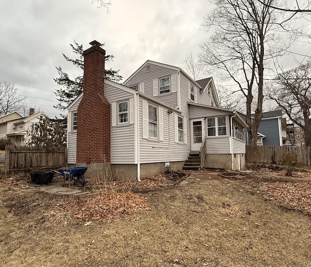 rear view of house with entry steps, a sunroom, a chimney, and fence