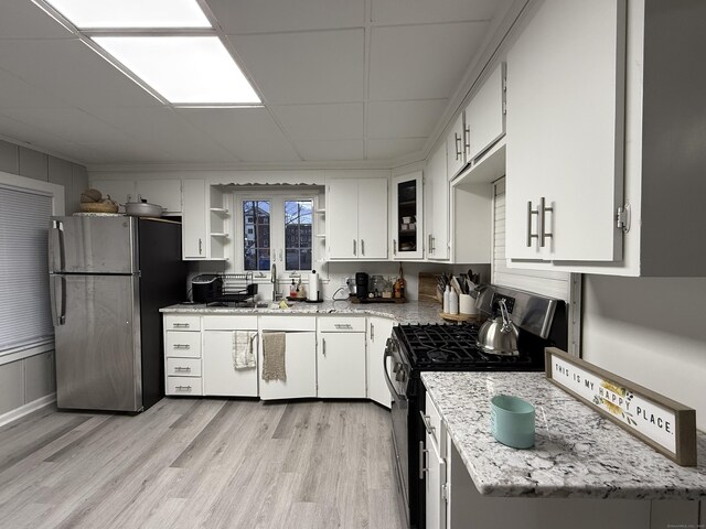 kitchen with open shelves, light stone countertops, light wood finished floors, stainless steel appliances, and white cabinetry