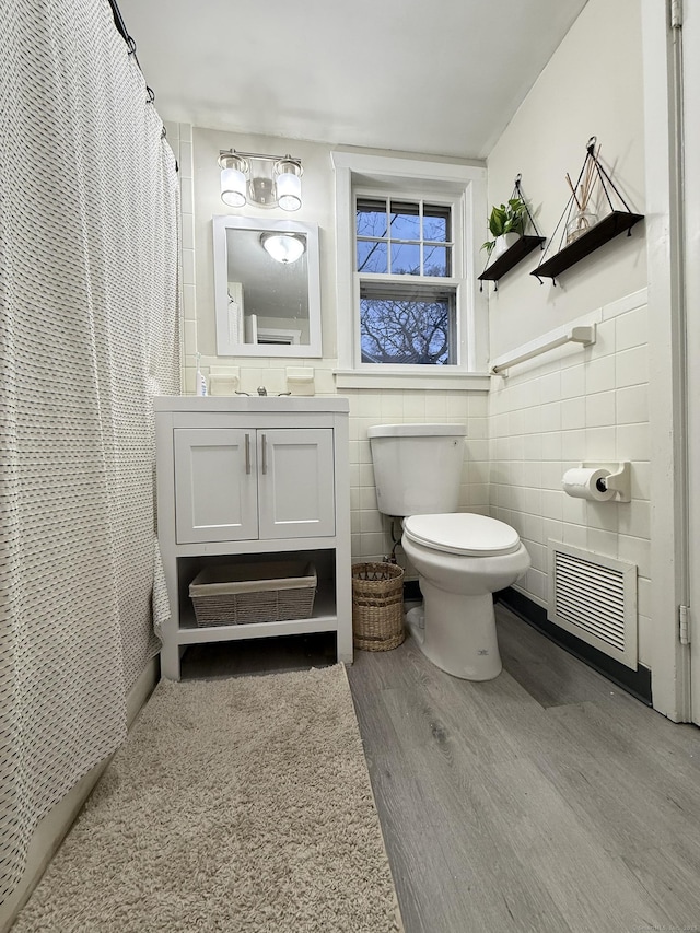 full bathroom with toilet, wood finished floors, vanity, visible vents, and tile walls