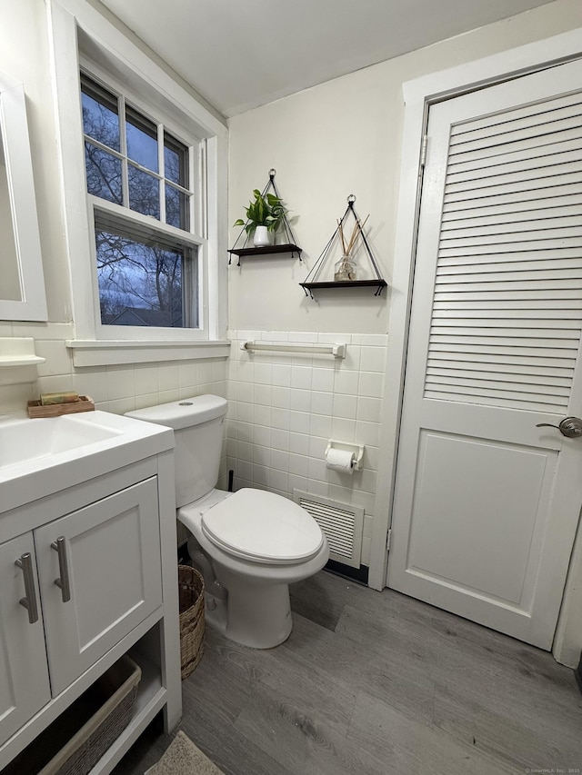 half bath with visible vents, toilet, a wainscoted wall, vanity, and tile walls