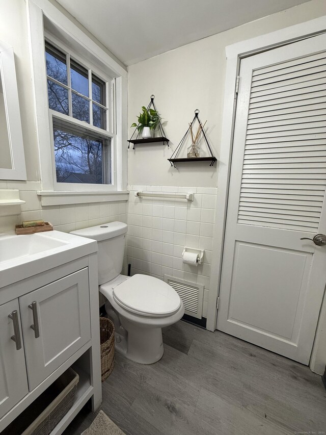 half bathroom featuring visible vents, tile walls, wood finished floors, vanity, and toilet