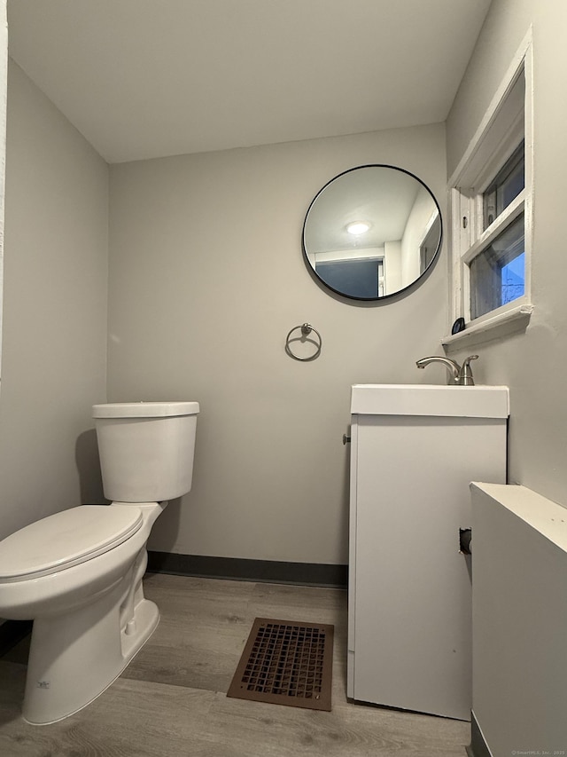 half bath with baseboards, visible vents, toilet, wood finished floors, and vanity