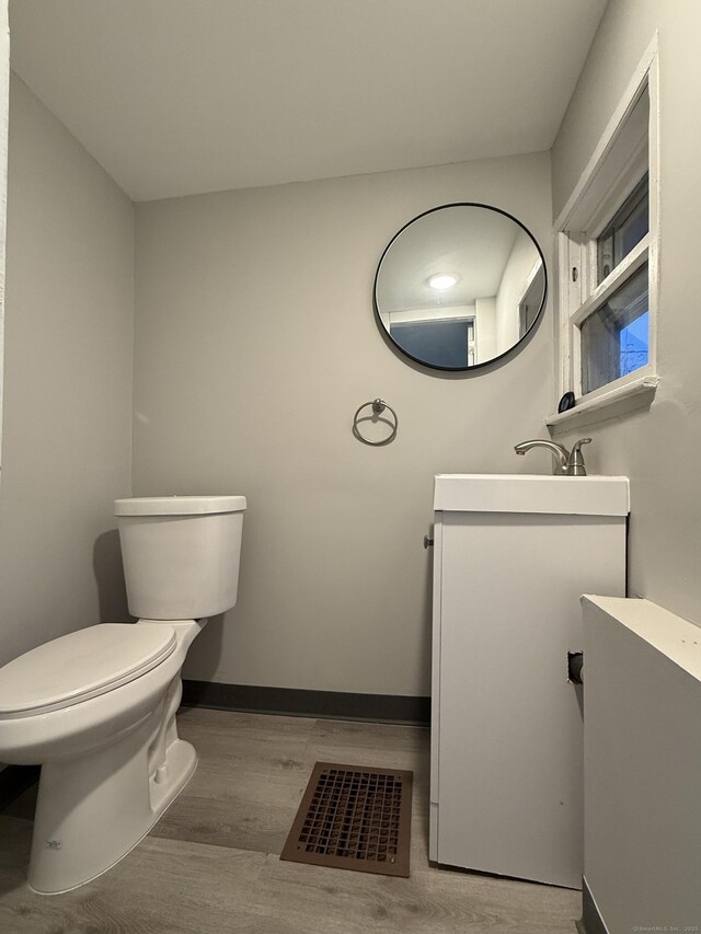 half bathroom with vanity, toilet, baseboards, wood finished floors, and visible vents