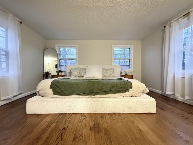 bedroom with a textured ceiling, dark wood-style flooring, and baseboards