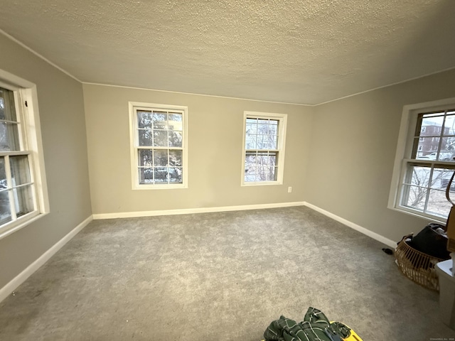 carpeted empty room featuring baseboards, a textured ceiling, and a healthy amount of sunlight