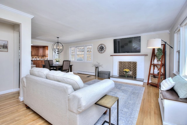 living room with light wood-style flooring, a notable chandelier, baseboard heating, a brick fireplace, and crown molding