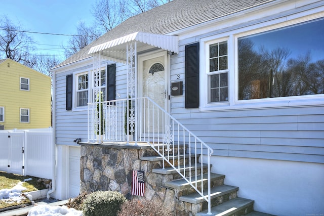 doorway to property with a shingled roof and fence