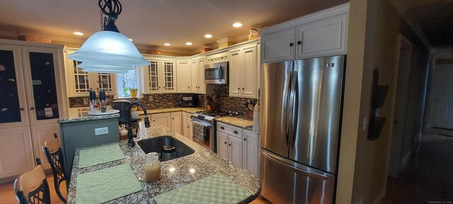 kitchen featuring a sink, appliances with stainless steel finishes, backsplash, light stone countertops, and glass insert cabinets