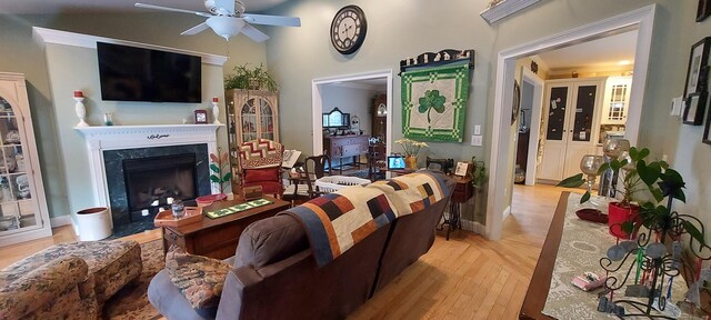 living area with a premium fireplace, light wood-type flooring, a towering ceiling, and a ceiling fan