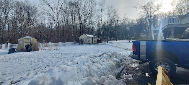 yard covered in snow featuring a shed, an outdoor structure, and fence