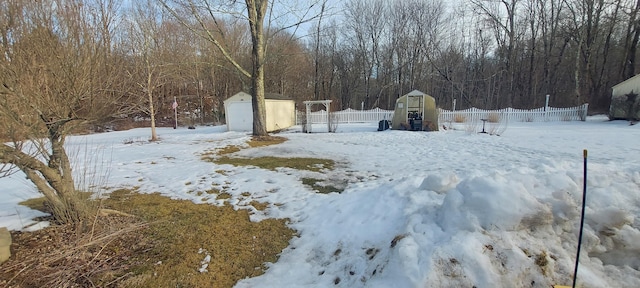 yard covered in snow featuring an outbuilding, fence, a view of trees, and a storage shed