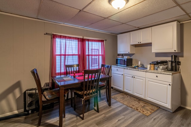 dining area featuring a drop ceiling, light wood-style flooring, and baseboards