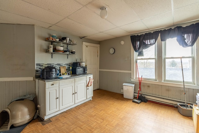 kitchen with black microwave, a paneled ceiling, a wainscoted wall, white cabinetry, and open shelves