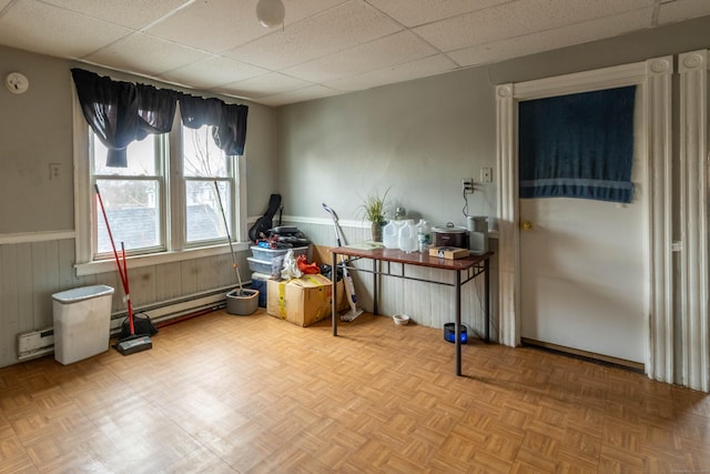 misc room with a paneled ceiling, wainscoting, a baseboard radiator, and wooden walls