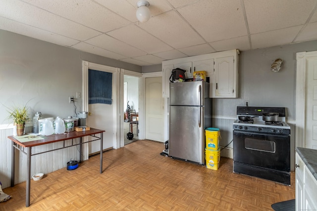 kitchen with a paneled ceiling, range with gas cooktop, freestanding refrigerator, and white cabinetry