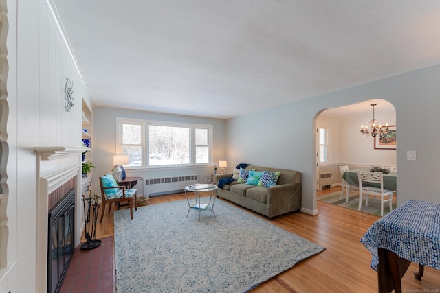 living area featuring arched walkways, dark wood-style flooring, a brick fireplace, and radiator