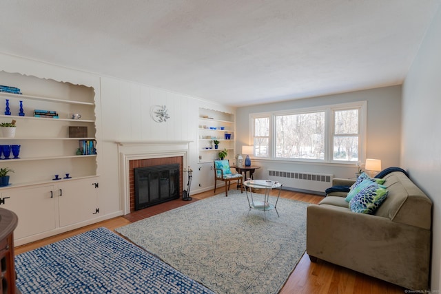 living area with built in features, light wood-type flooring, radiator, and a fireplace