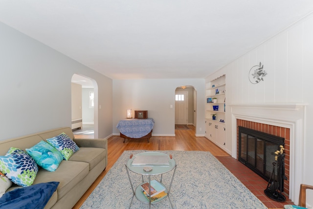 living room featuring arched walkways, radiator heating unit, a brick fireplace, and wood finished floors