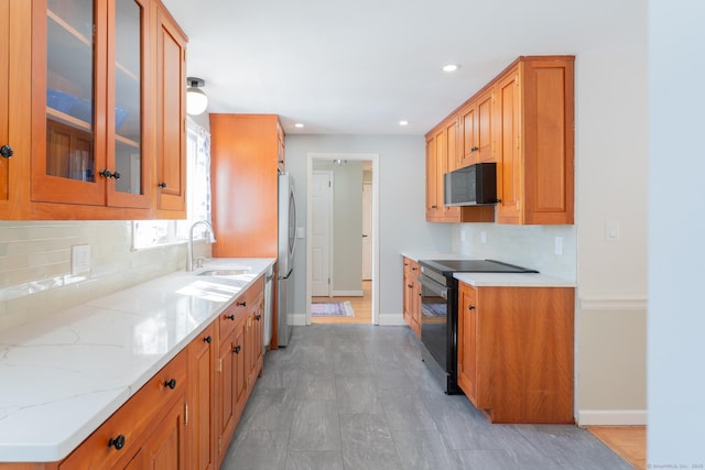 kitchen featuring tasteful backsplash, baseboards, light stone counters, black appliances, and a sink