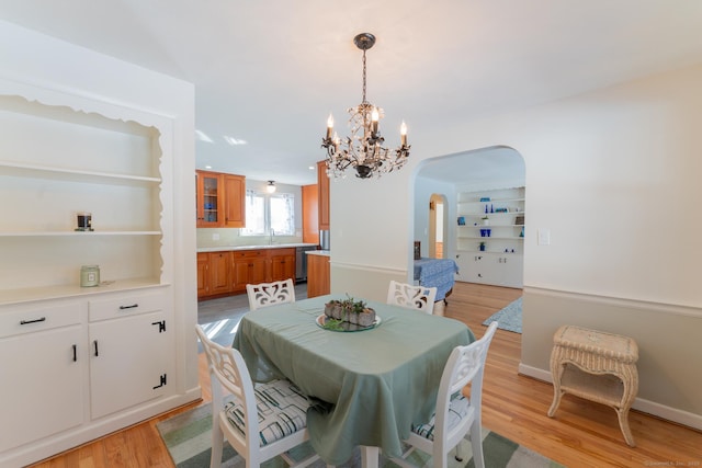 dining room with light wood-style flooring, arched walkways, a chandelier, and baseboards