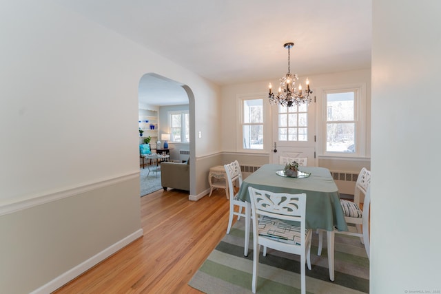 dining space featuring light wood-style floors, arched walkways, radiator, and baseboards