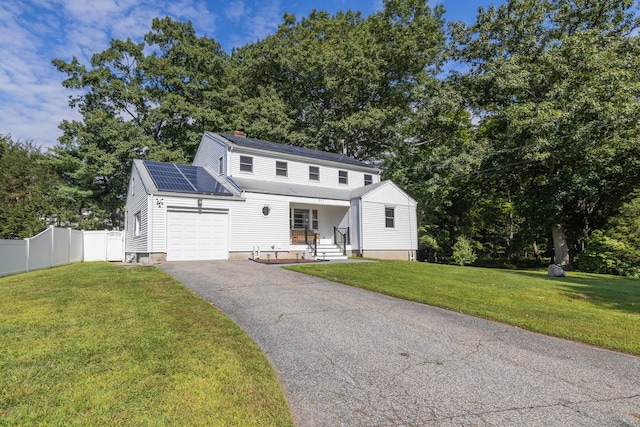 view of front of house with an attached garage, fence, driveway, roof mounted solar panels, and a front yard