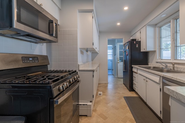 kitchen with appliances with stainless steel finishes, light countertops, white cabinetry, a sink, and recessed lighting