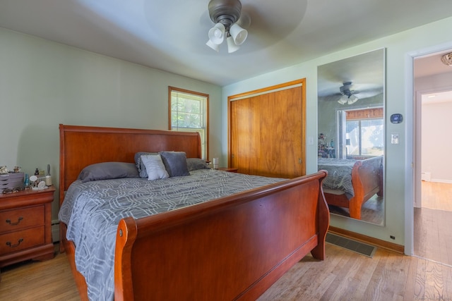 bedroom featuring light wood finished floors, ceiling fan, visible vents, and a baseboard heating unit