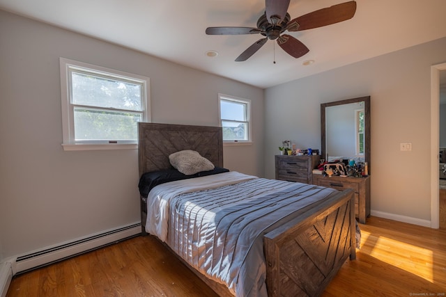 bedroom with a baseboard heating unit, multiple windows, and light wood finished floors