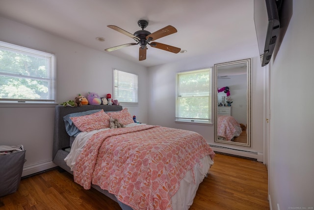 bedroom featuring multiple windows, baseboard heating, a baseboard radiator, and wood finished floors