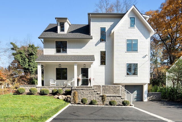 shingle-style home with driveway, a garage, a shingled roof, covered porch, and a front lawn