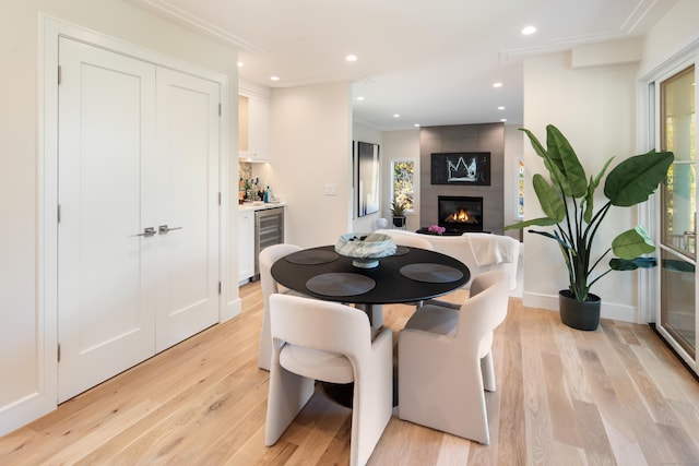 dining room featuring a wealth of natural light, wine cooler, a large fireplace, and light wood-style flooring