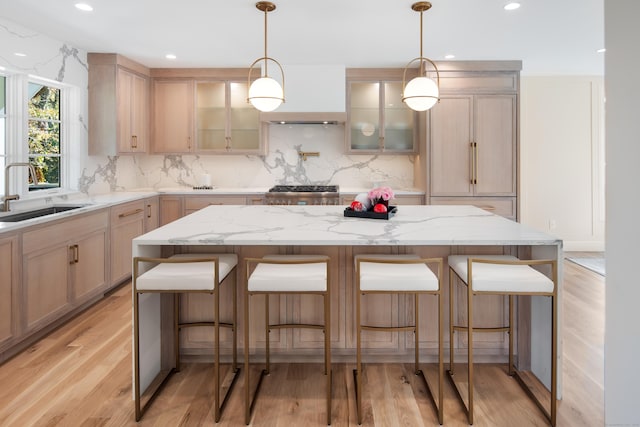 kitchen featuring backsplash, a sink, light wood-style flooring, and a kitchen breakfast bar