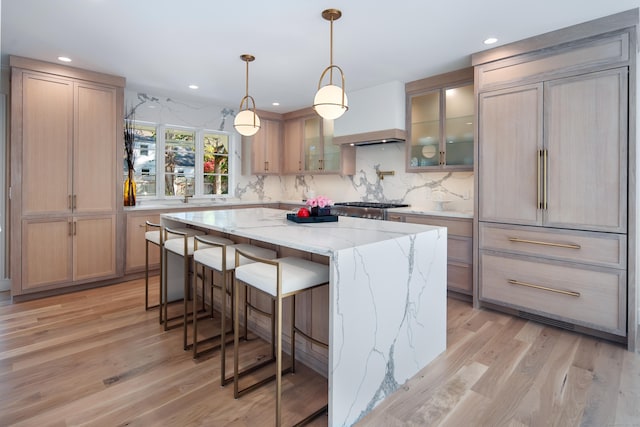 kitchen with a breakfast bar area, a kitchen island, light wood-type flooring, light stone countertops, and glass insert cabinets